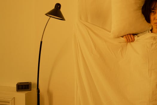 Personne allongée dans un lit avec des draps blancs, lampe douce à côté et réveil affichant 3h33.