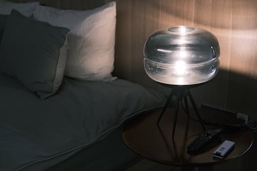 Lampe douce éclairant une table de nuit avec un lit en arrière-plan, créant une ambiance apaisante avant le coucher.